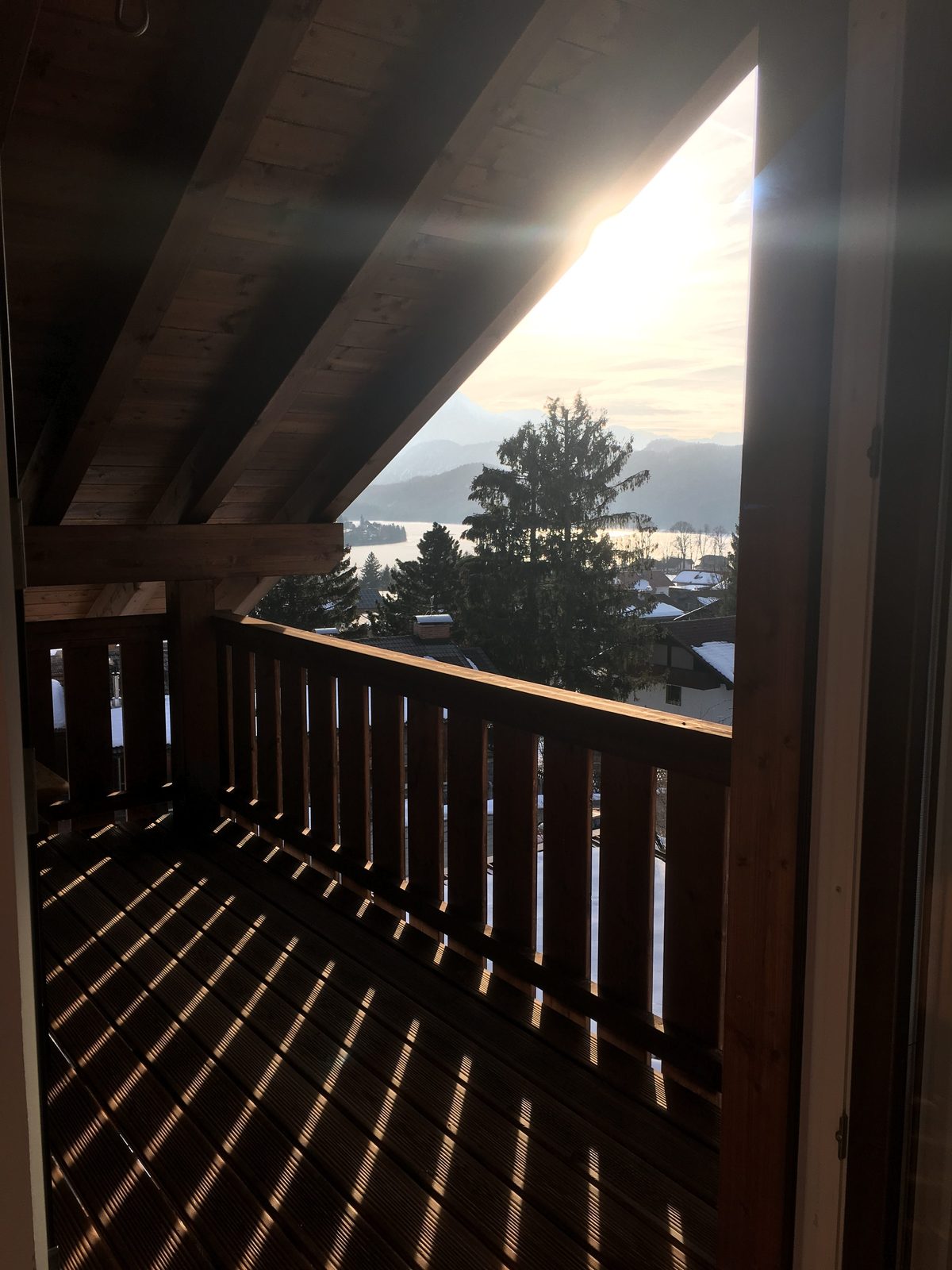 Holzbalkon im Gegenlicht der Sonne mit Blick auf Bäume und Berge
