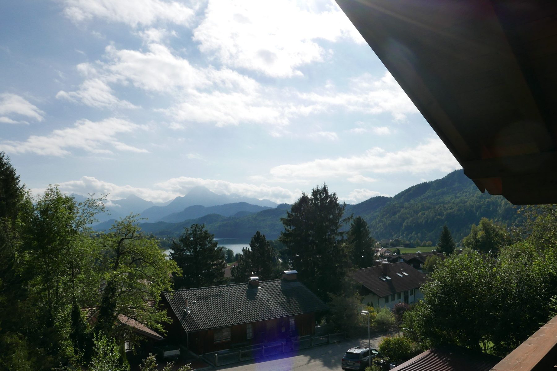 Blick vom Balkon über Dächer und Wald auf den Weißensee und die Berge