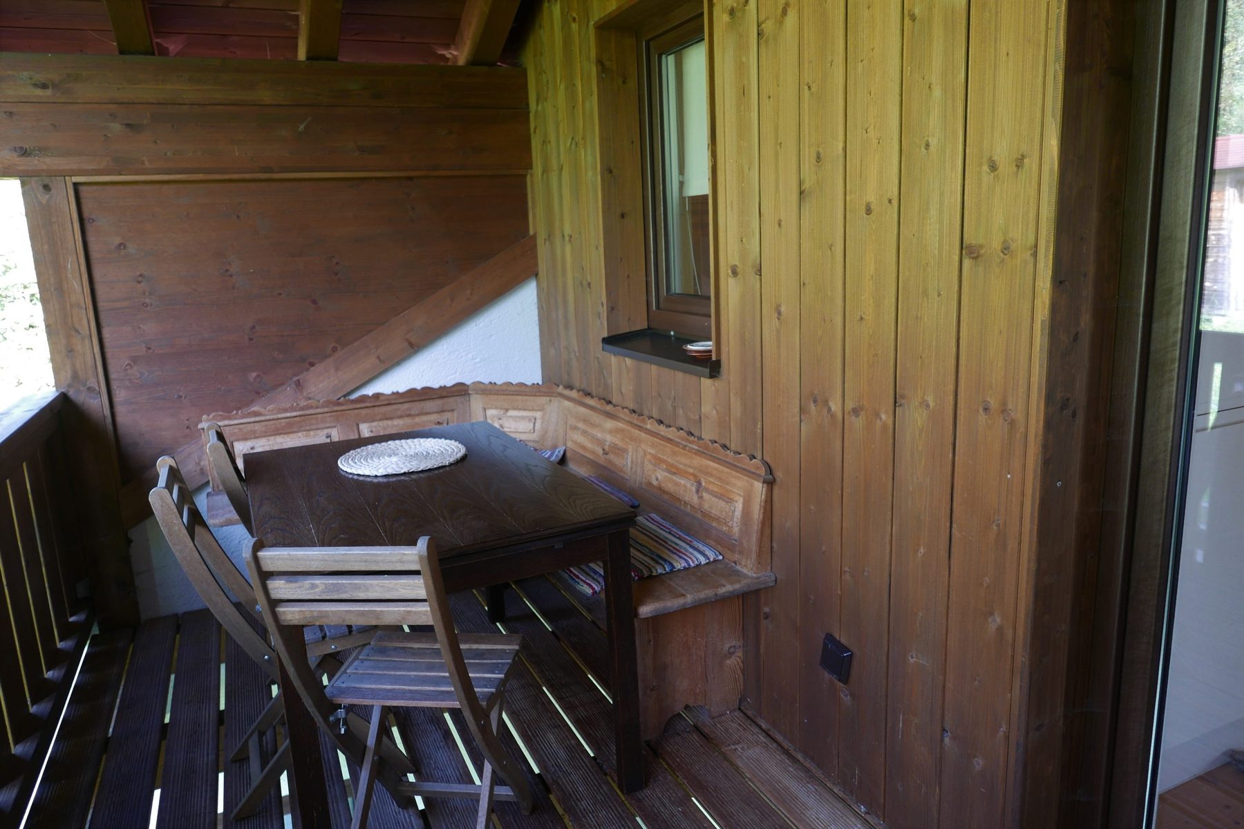 Überdachter Balkon mit Holzbank, Tisch und Stühlen zum Essen im Freien