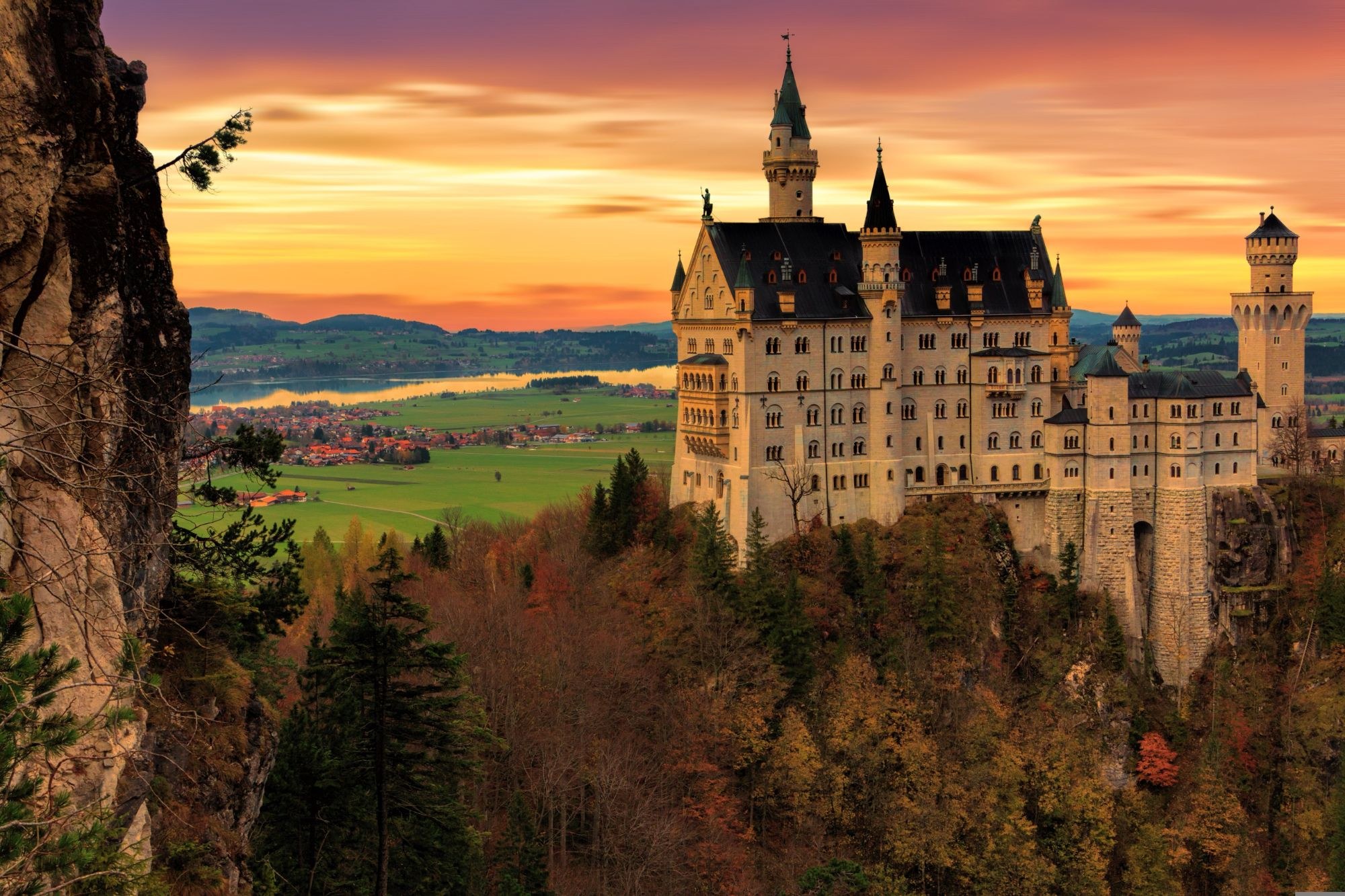 Schloss Neuschwanstein im Herbst bei Sonnenuntergang, im Tal dahinter Dörfer und der Forggensee