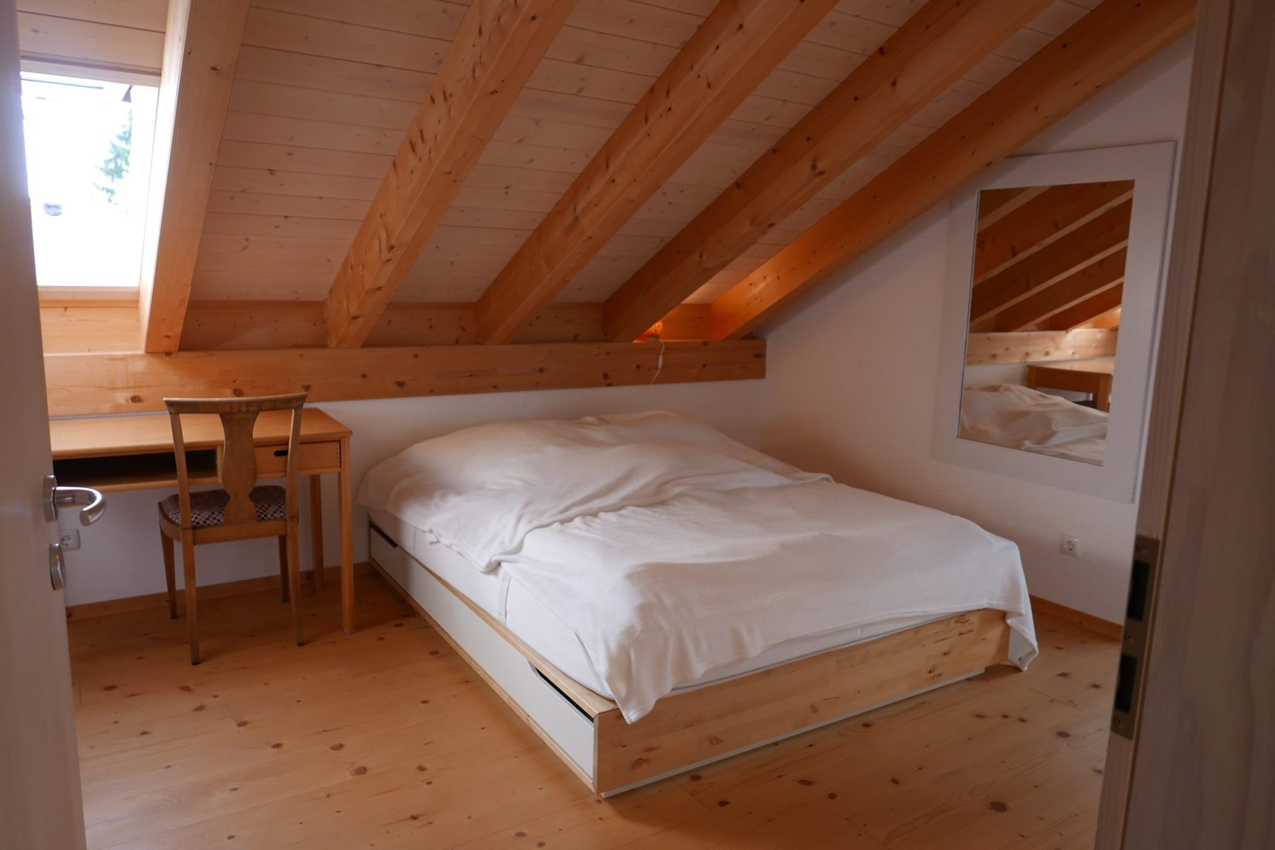 Schlafzimmer eins mit Schreibtisch am Fenster und weiß bezogenem Doppelbett