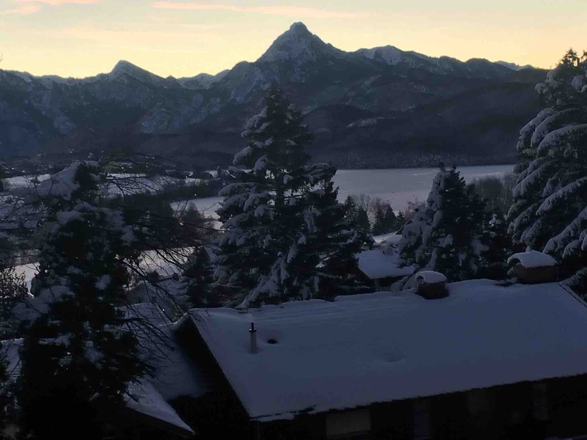 Verschneite Dächer und Tannen im Abendlicht, dahinter die Bergkette