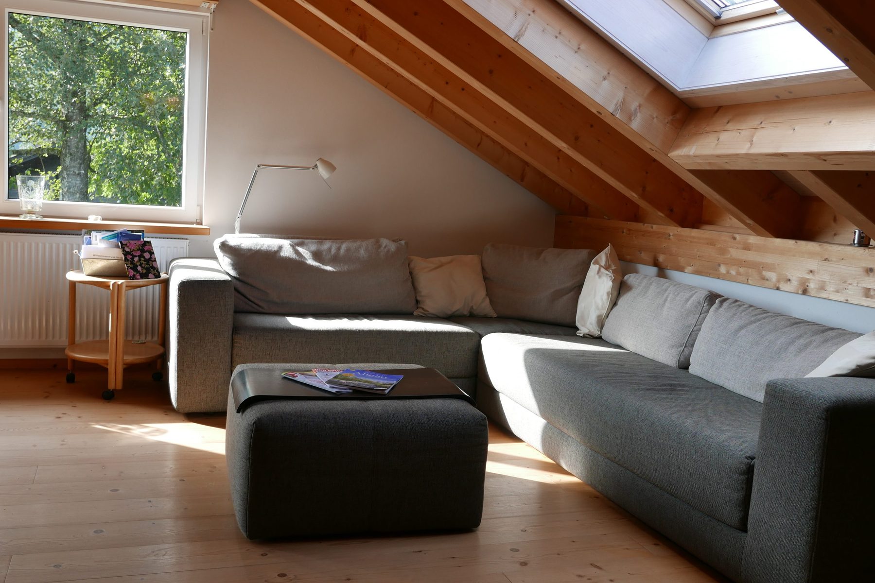 Graues Ecksofa mit Polsterhocker und Leselampe unter Dachfenstern